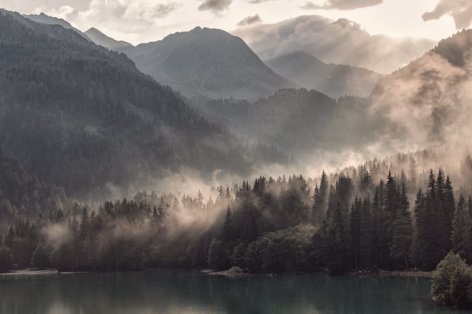Brume qui se lève sur un lac de montagne, au pied de sommets boisés
